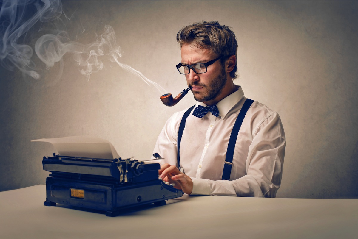 Picture of a man using a writing machine and smoking with a pipe